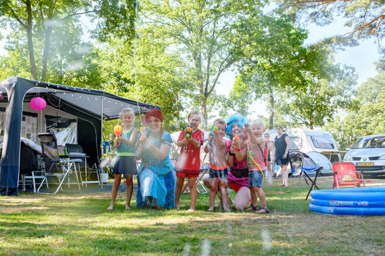 Kinderen en volwassenen spelen met waterpistolen voor een glampingtent op een zomerse camping.