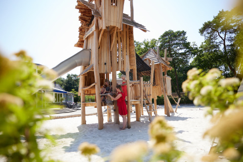 Parque infantil de madera en un alojamiento glamping, con niños, adulto y naturaleza alrededor.