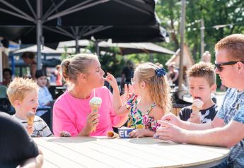 A family enjoys ice cream together at a round outdoor table near a safari tent café on a sunny day.
