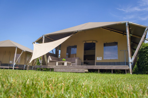 Safari Cottage Safarizelt mit Veranda im Ferienpark De Boshoek, Niederlande, unter blauem Himmel.