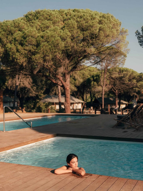 Person slapper af i poolen i Wecamp Cádiz feriepark i Andalusien, Spanien, omgivet af fyrretræer.