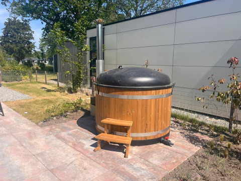 Houten hottub met zwart deksel en trapje naast een moderne lodge in Zuiderzee, Nederland.