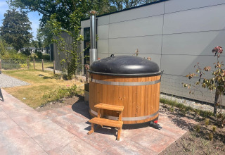 Houten hottub met zwart deksel en trapje naast een moderne lodge in Zuiderzee, Nederland.
