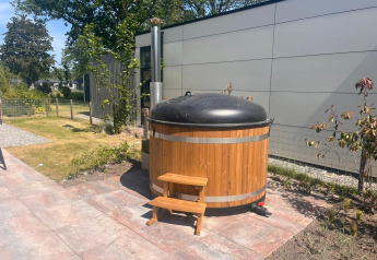 Houten hottub met zwart deksel en trapje naast een moderne lodge in Zuiderzee, Nederland.