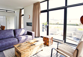 Salon moderne lumineux avec de grandes fenêtres au lodge L-Cube à Zuiderzee, Pays-Bas, vue sur la terrasse.