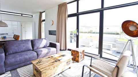 Heldere, moderne woonkamer met grote ramen in de L-Cube lodge aan de Zuiderzee, Nederland, zicht op terras.