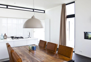 Moderne eetruimte en keuken in L-Cube-lodge aan de Zuiderzee, Nederland, met bruine stoelen.