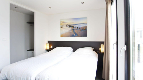 Lichte hedendaagse slaapkamer in L-Cube lodge bij de Zuiderzee, Nederland, met grote ramen en een strak interieur.