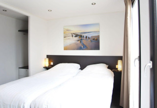 Lichte hedendaagse slaapkamer in L-Cube lodge bij de Zuiderzee, Nederland, met grote ramen en een strak interieur.