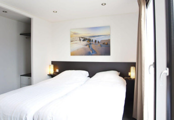 Lichte hedendaagse slaapkamer in L-Cube lodge bij de Zuiderzee, Nederland, met grote ramen en een strak interieur.