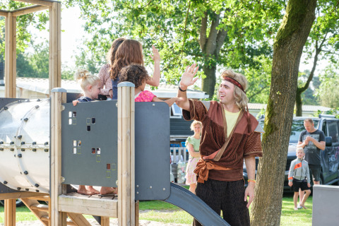 Kinder spielen auf einem Spielplatz mit einem verkleideten Animateur bei einer Glamping-Unterkunft.
