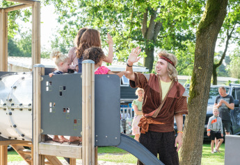 Des enfants jouent sur une aire de jeux avec un animateur déguisé dans un hébergement glamping en plein air.