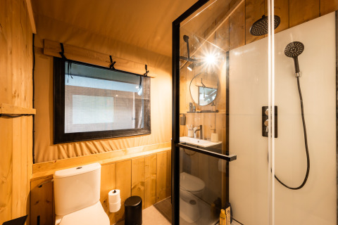 Modern bathroom in a safari tent featuring wood-paneled walls, a window, shower enclosure, and toilet.