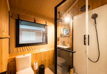 Baño moderno en una tienda safari con paredes de madera, ventana, cabina de ducha y sanitario blanco.