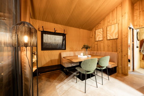 Eethoek in een luxe safaritent met houten wanden en stijlvolle meubels bij Kampeerdorp de Zandstuve.