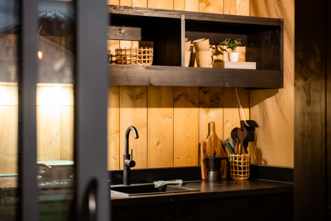 Moderne keukenhoek in een safaritent met houten wandbekleding, open rekken en zwarte kraan.