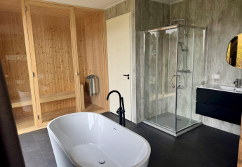 Moderne badkamer in Modus Wellness 2 lodge met vrijstaand bad, glazen douche, sauna en wastafel.