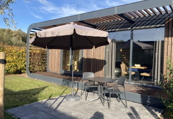 Udendørs terrasse ved Modus Wellness 2-lodgen i Zuiderzee, Holland, med bord, stole og stor parasol.