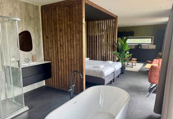 Moderne lodge Modus Wellness 2 bij Zuiderzee, Nederland, met vrijstaand bad, bed en strakke keuken.