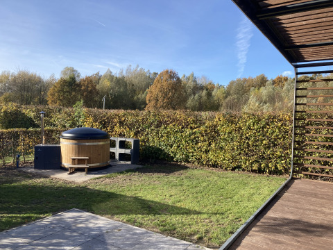 Gartenansicht mit Whirlpool bei Modus Wellness 2, Zuiderzee, Niederlande, umgeben von Hecken und Bäumen.