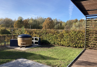 Gartenansicht mit Whirlpool bei Modus Wellness 2, Zuiderzee, Niederlande, umgeben von Hecken und Bäumen.
