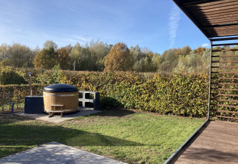 Tuin en bubbelbad aan Modus Wellness 2, Zuiderzee, Nederland, met groene hagen en bomen op de achtergrond.