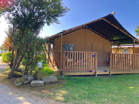 Tenda safari con veranda privata e servizi igienici, immersa nel verde sotto un cielo azzurro.