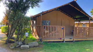 Tenda safari con veranda privata e servizi igienici, immersa nel verde sotto un cielo azzurro.