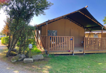 Safari tent with private veranda and sanitary facilities, nestled in greenery under a clear blue sky.