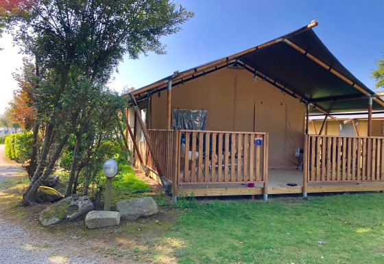 Safari tent with private veranda and sanitary facilities, nestled in greenery under a clear blue sky.
