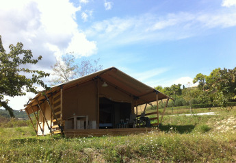 Safari tent with sanitary facilities in a grassy field, surrounded by trees and under a blue sky.