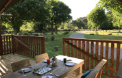 View from a safari tent terrace with wooden table at Camping de Kerleyou, France, surrounded by greenery.