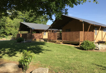 Tenda safari con servizi igienici al Camping de Kerleyou in Francia, circondata da prato e alberi.
