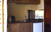 Et lille køkken med træskabe, gaskomfur og minikøleskab i et safaritelt på Camping Podere sei Poorte.