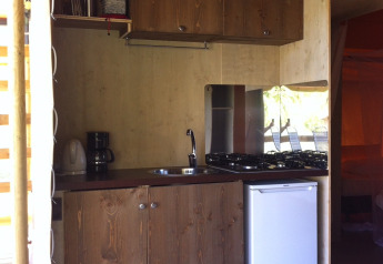 Compact kitchen with wooden cabinets, gas stove, and mini fridge inside a safari tent at Camping Podere sei Poorte.