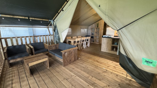 Intérieur d’une tente safari avec terrasse en bois, salon, grande table à manger et coin cuisine.