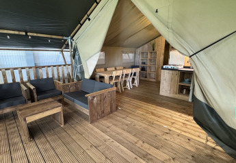 Gezellige safari tent interieur met houten vloer, zithoek, eettafel en keukenhoek met sanitair.
