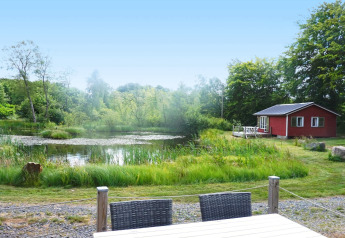 Idyllischer Blick auf einen Teich und ein rotes Ferienhaus für 4 Personen in SMEDSTORP, umgeben von Natur.