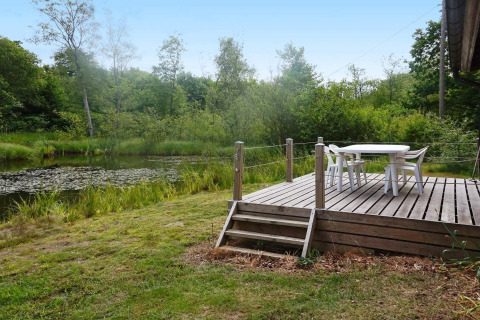 Udendørs træterrasse med havebord og stole ved en fredelig dam, omgivet af frodig svensk natur.