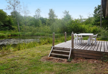 Terrazza in legno con tavolo e sedie bianche vicino a uno stagno, circondata dal verde in Svezia.