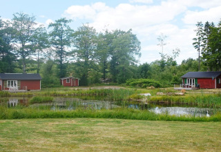 Cabañas rojas de vacaciones junto a un estanque rodeado de naturaleza en SMEDSTORP, Suecia, en un día soleado.