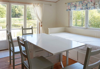 Sala da pranzo luminosa con ampie finestre, tavolo, sedie e divano letto nel lodge Smedstorp, Svezia.