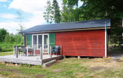 Rotes Ferienhaus mit grünen Fensterläden, Terrasse und Gartenmöbeln in Smedstorp, Schweden.