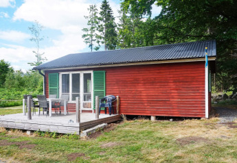 Rotes Ferienhaus mit grünen Fensterläden, Terrasse und Gartenmöbeln in Smedstorp, Schweden.