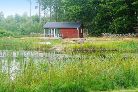 Petite maison de vacances rouge au bord d’un étang à SMEDSTORP, Suède, idéale pour 4 personnes en pleine nature.