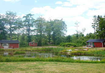 Wunderschönes rotes Ferienhaus am Teich, umgeben von Natur, bei Smedstorp in Schweden, sonniger Tag.