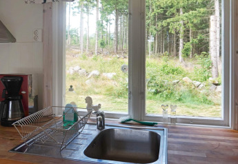 Küche mit Spüle, Geschirrkorb, Kaffeemaschine und Ausblick auf den Wald durch Fenster in Smedstorp, Schweden.
