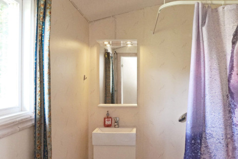 Badezimmer in einem Ferienhaus in Smedstorp, Schweden, mit Spiegel, Waschbecken, Fenster und Duschvorhang.