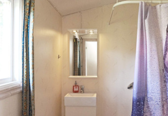 Badezimmer in einem Ferienhaus in Smedstorp, Schweden, mit Spiegel, Waschbecken, Fenster und Duschvorhang.