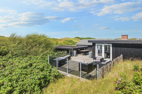 Terrasse der Seaside Charm Lodge in Rindby, umgeben von Dünen und Natur unter blauem Himmel.